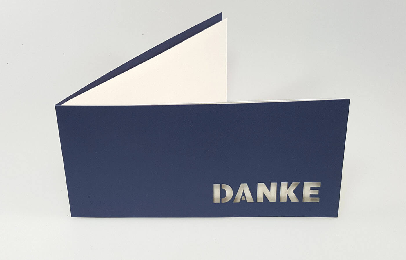 Dunkelblaue Dankkarte DIN lang mit ausgestanztem Schriftzug "Danke" in Schreibschrift und weißem Einlegeblatt - aufgestellt