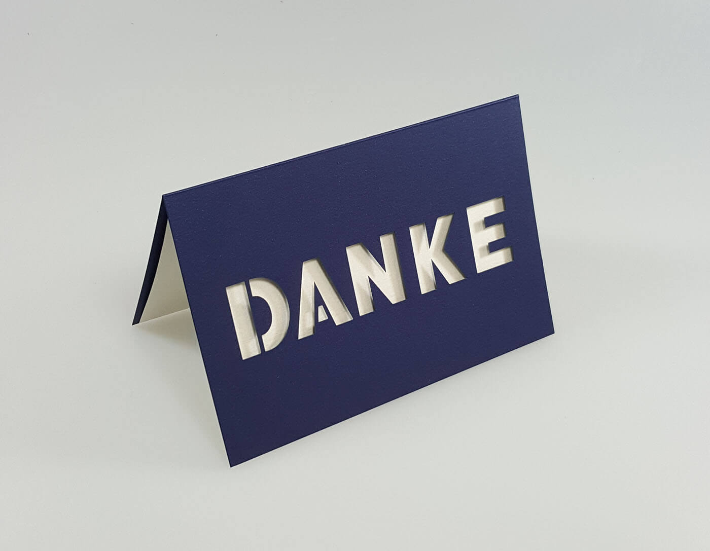 Dunkelblaue Dankkarte mit zentral ausgestanztem Schriftzug "DANKE" und weißem Einlegeblatt - Aufgestellte Ansicht