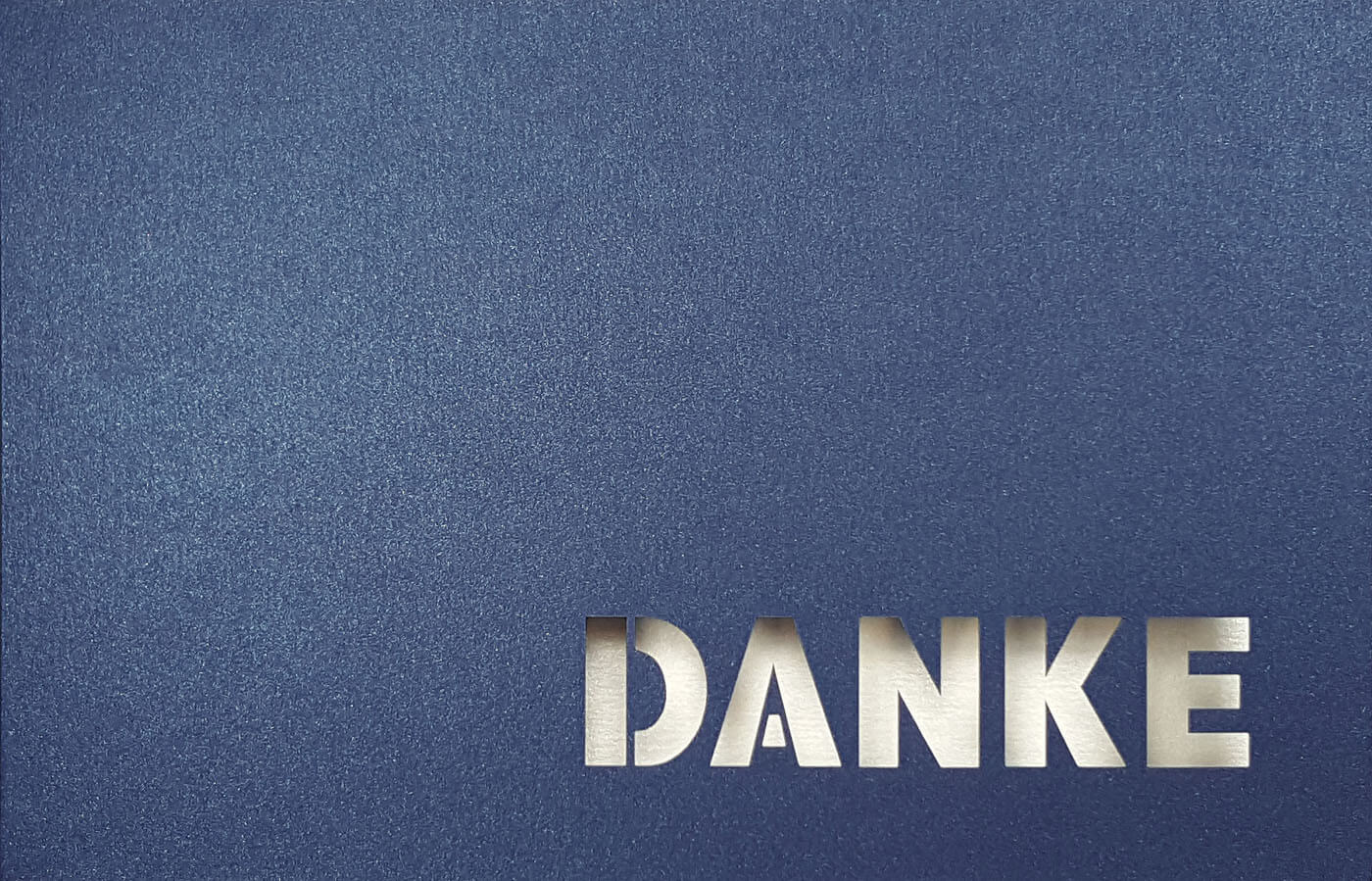 Dunkelblaue Danksagungskarte querdoppelt mit ausgestanztem Schriftzug "DANKE" und weißem Einlegeblatt