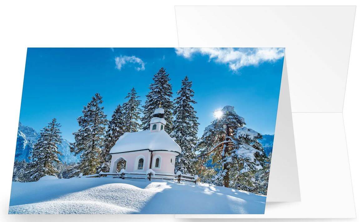 Winter-Weihnachtskarte mit verschneiter, romantischer Bergkapelle und hohen Tannen