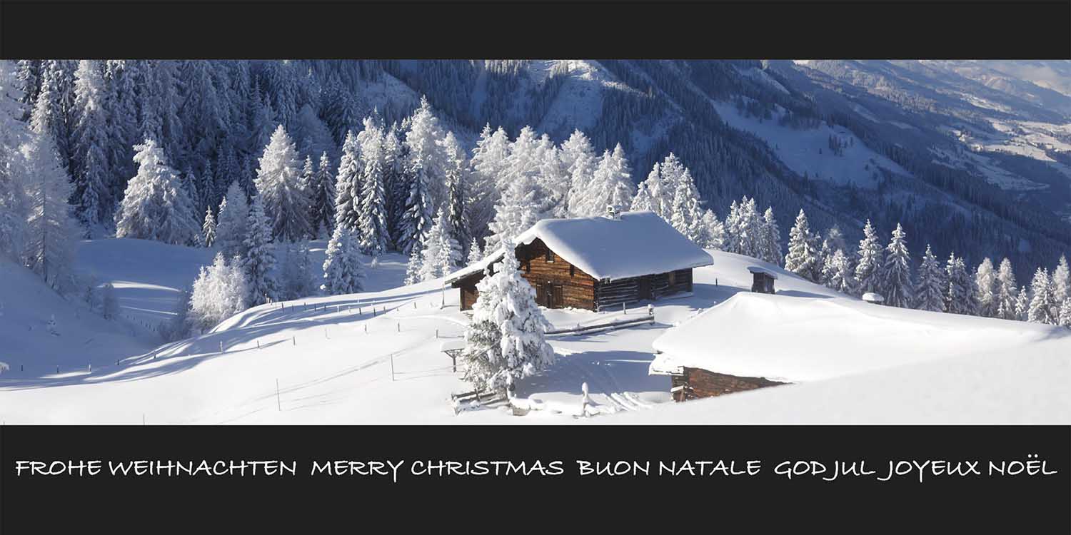 Winterliche Weihnachtskarte mit verschneiter Alm-Hütte in alpenländischer Berglandschaft und Schriftzug "Frohe Weihnachten" in verschiedenen Sprachen