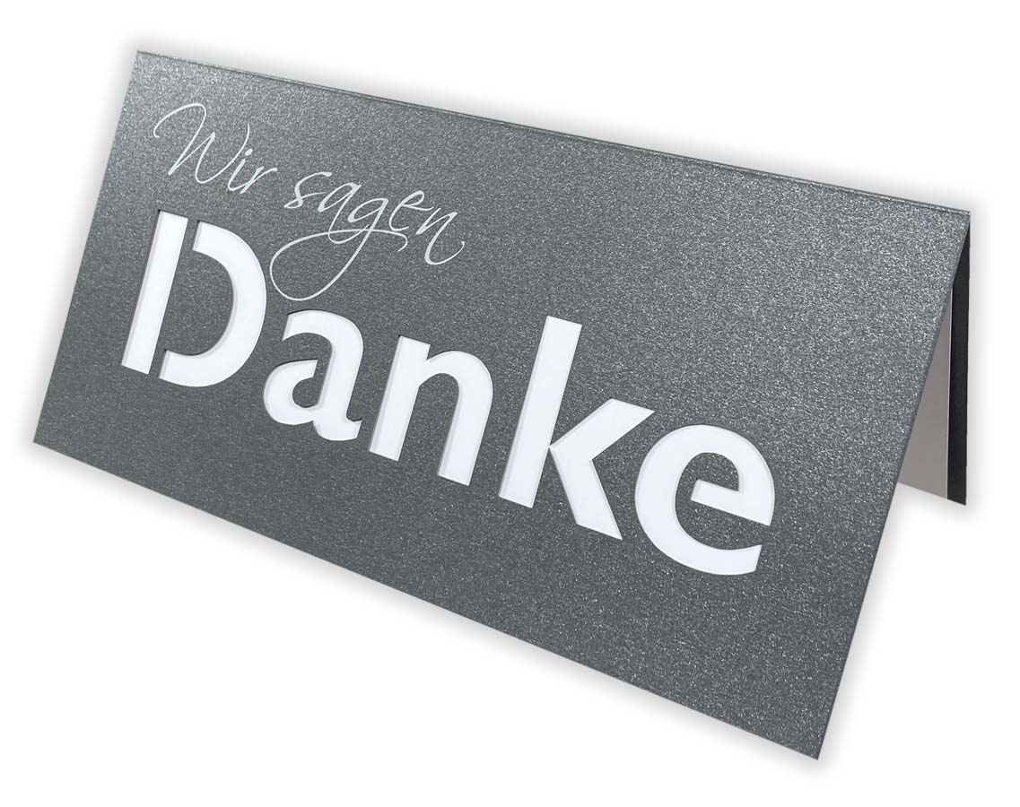 Anthrazitgraue Dankkarte DIN lang mit gedrucktem "Wir sagen", ausgestanztem Schriftzug "Danke" und passenden Einlegeblatt