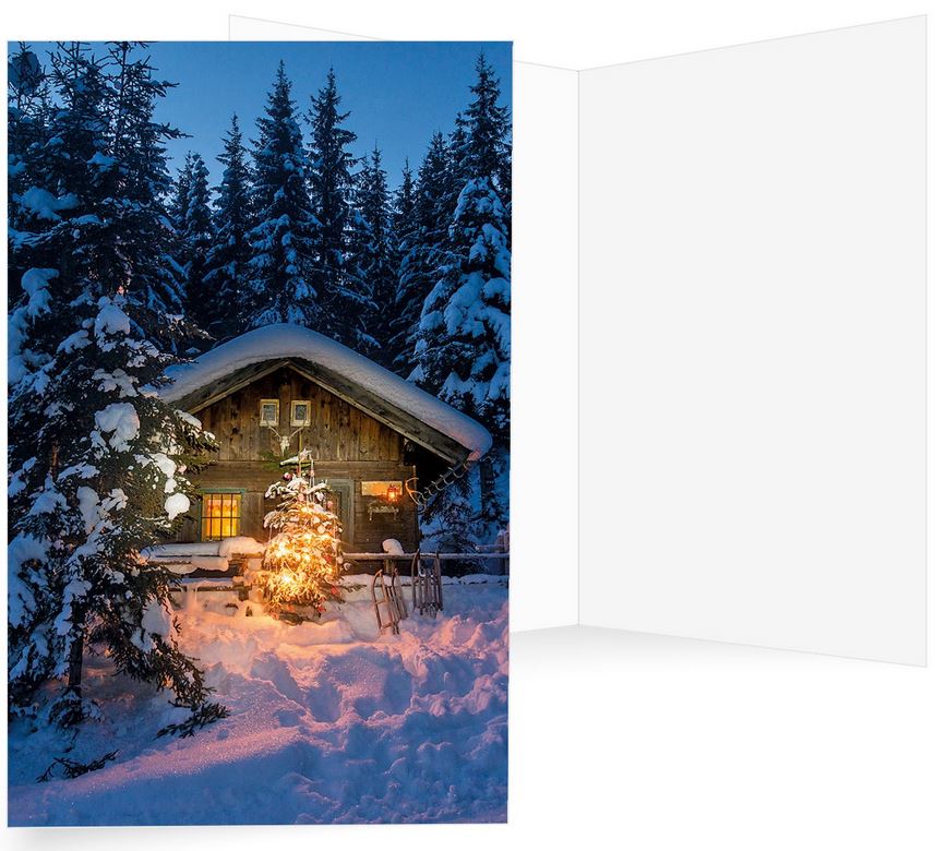 Winterliche Weihnachtskarte mit verschneitem Holzhaus zwischen hohen Tannen sowie Weihnachtsbaum