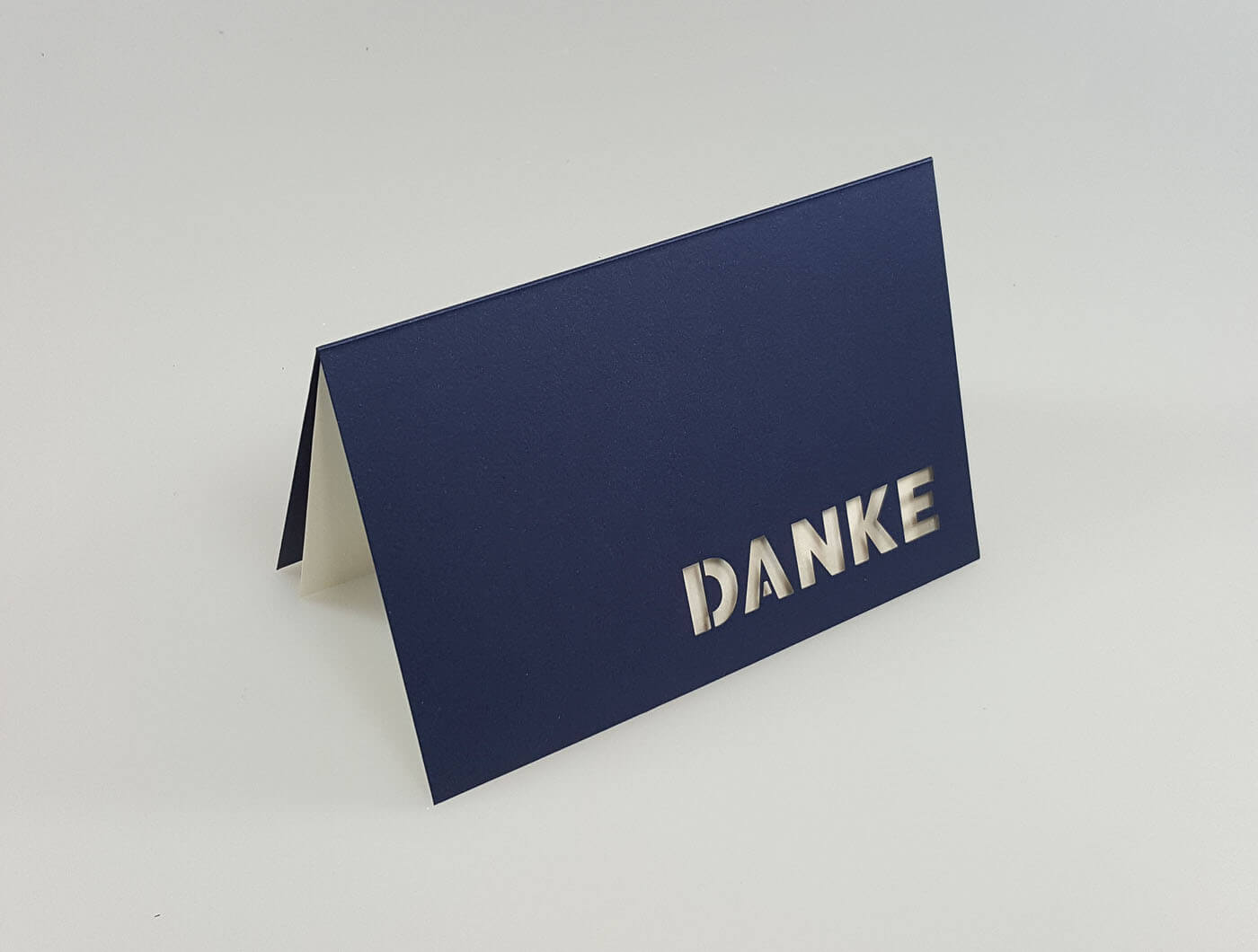 Dunkelblaue Dankkarte mit ausgestanztem Schriftzug "DANKE" und weißem Einlegeblatt - Aufgestellte Ansicht