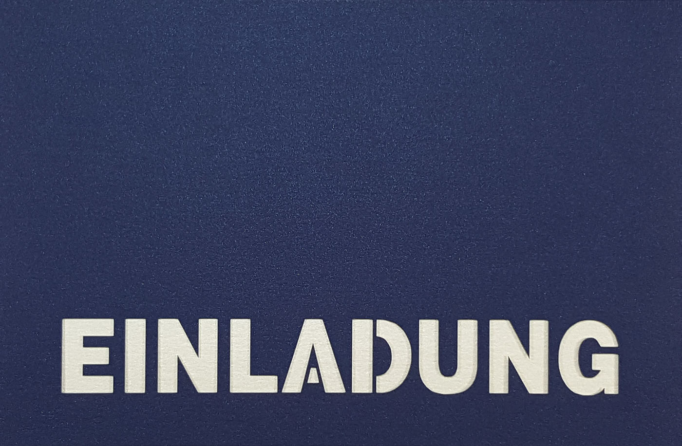 Dunkelblaue Einladungskarte mit ausgestanztem Schriftzug "EINLADUNG" und weißem Einlegeblatt