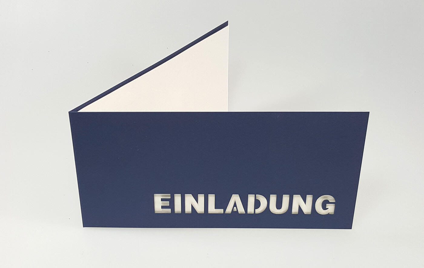 Dunkelblaue Einladungskarte DIN lang mit ausgestanztem Schriftzug "Einladung" und weißem Einlegeblatt - aufgestellt