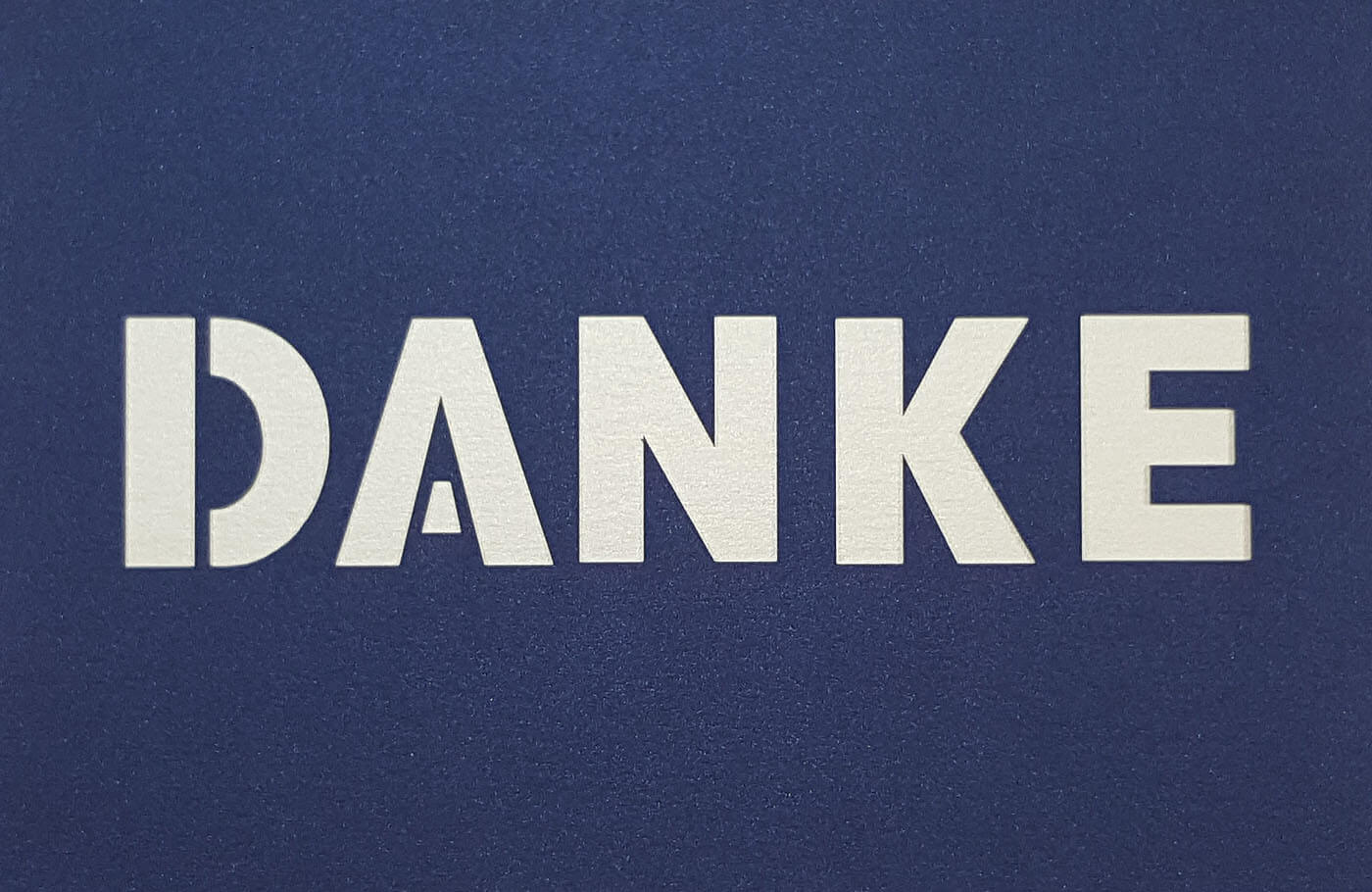 Dunkelblaue Danksagungskarte mit zentral ausgestanztem Schriftzug "DANKE" und weißem Einlegeblatt