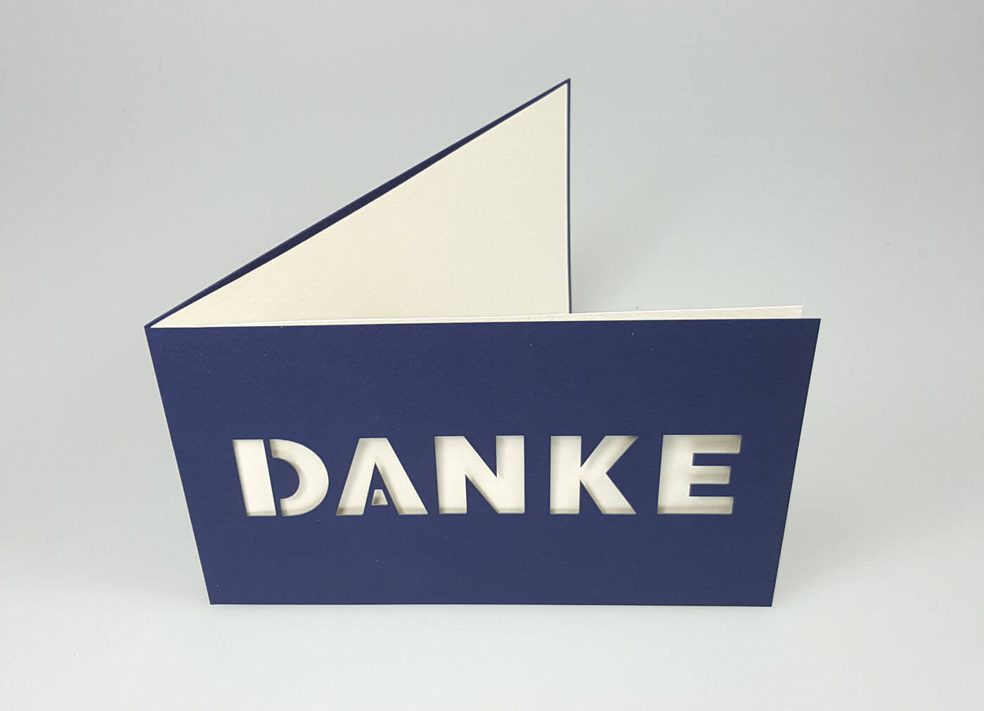 Dunkelblaue Dankkarte querdoppelt mit zentral ausgestanztem Schriftzug "DANKE" und weißem Einlegeblatt - Aufgestellte Ansicht