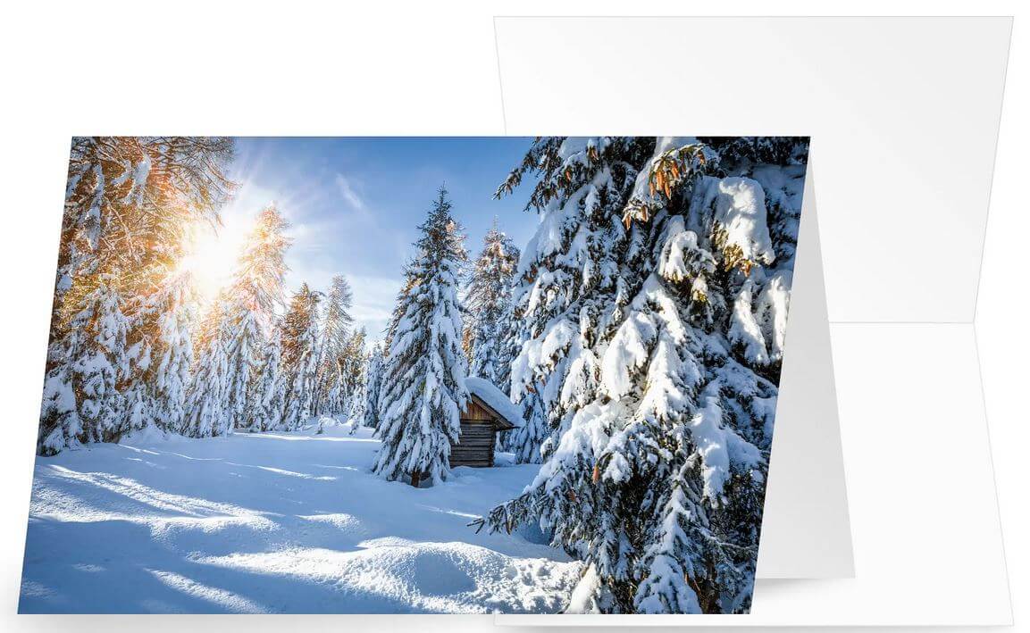 Winter-Weihnachtskarte "Neuschnee" mit verschneitem Wald, kleiner Hütte und Sonnenstrahlen