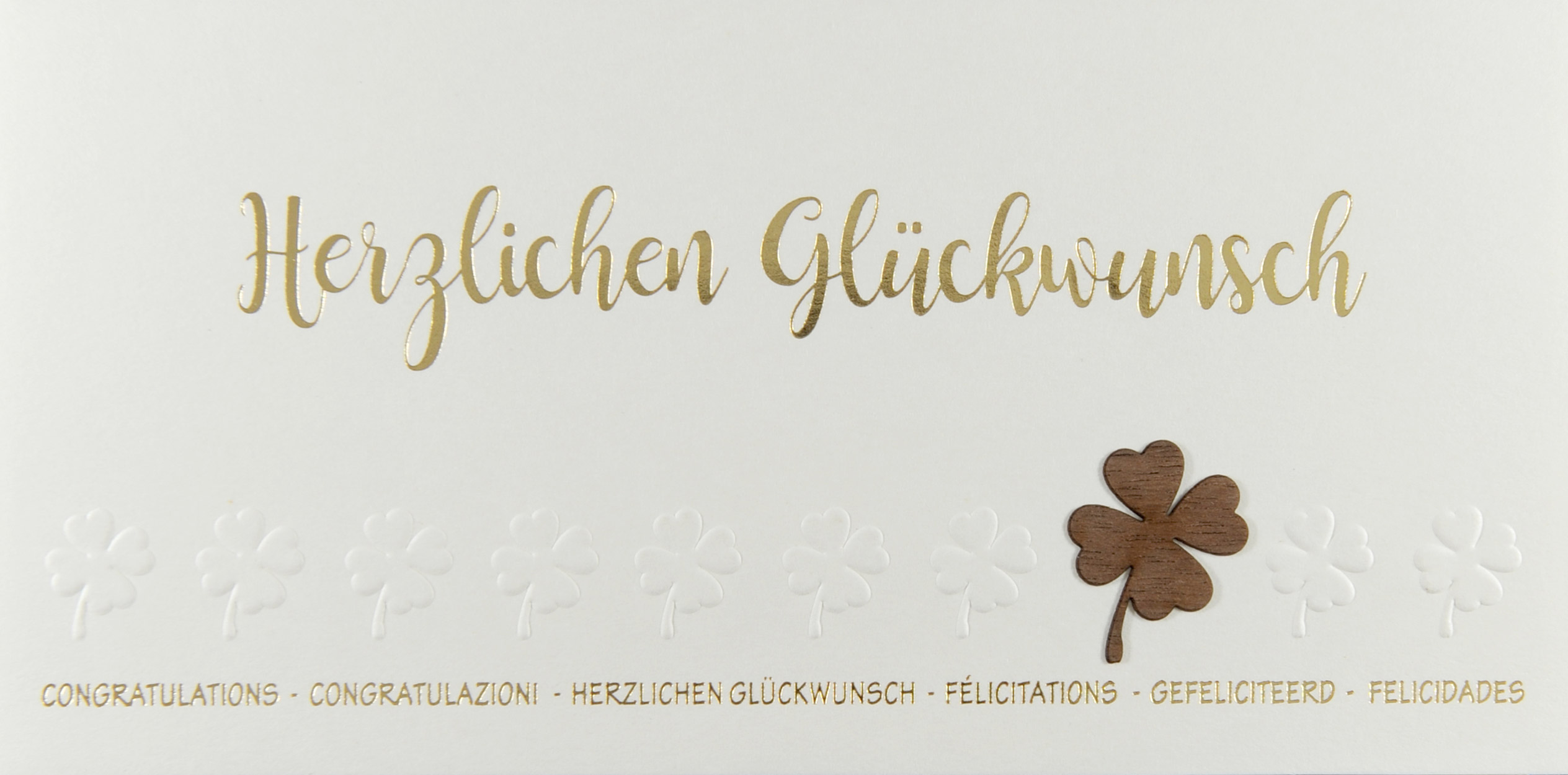 Mehrsprachige Glückwunschkarte mit Gold- und Blindprägung sowie einem aufgeklebtem Kleeblatt aus Holz.