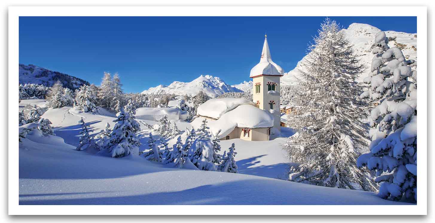 Winterliche Grußkarte im Panorama-Format mit verschneiter Kirche, Tannenbäumen und blauem Himmel