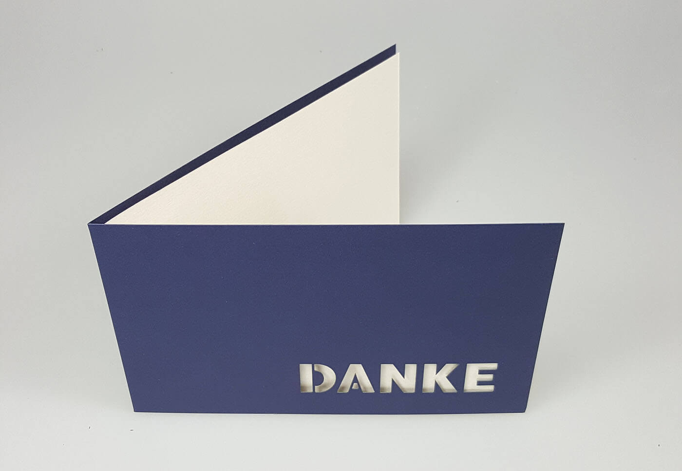 Dunkelblaue Dankkarte querdoppelt mit ausgestanztem Schriftzug "DANKE" und weißem Einlegeblatt - Aufgestellte Ansicht