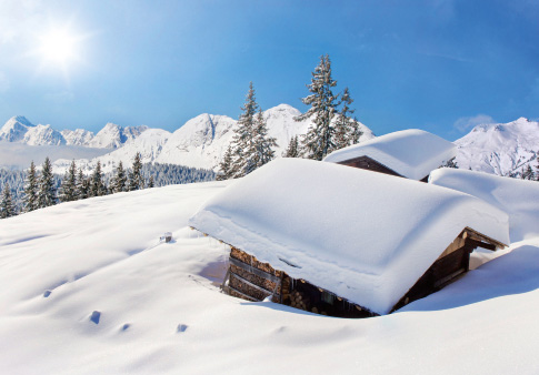 Weihnachtskarte mit verschneiten Berghütten unter blauem Himmel mit strahlender Sonne