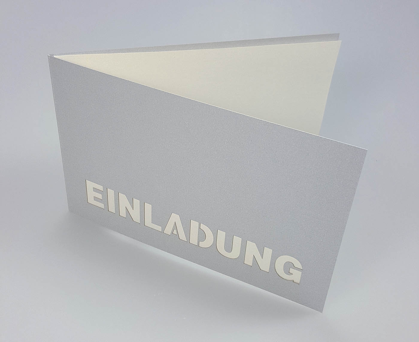 Silberne Einladungskarte mit ausgestanztem Schriftzug "EINLADUNG" und perlmutt Einlegeblatt - aufgeklappt