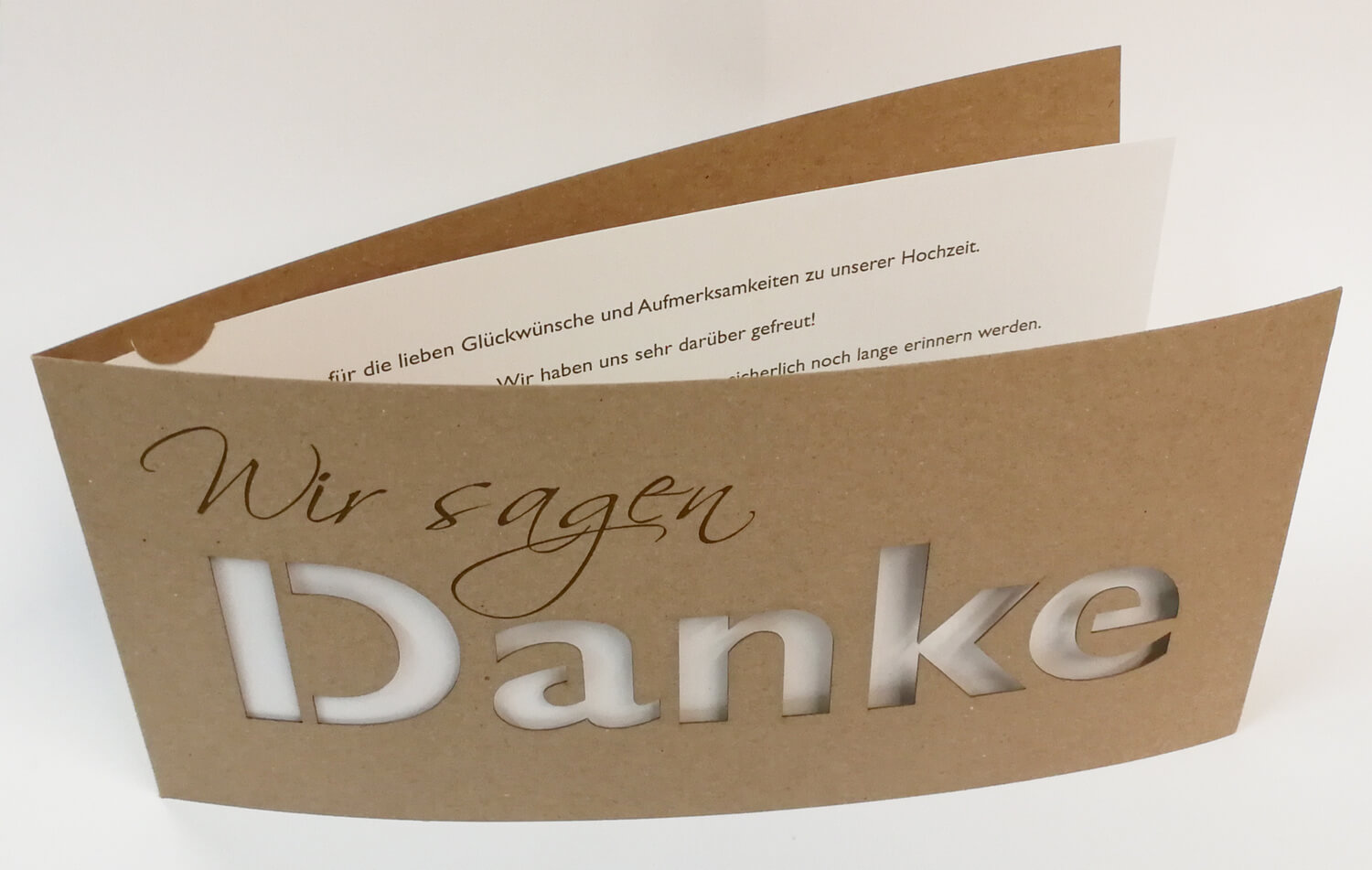 Braune Dankkarte DIN lang mit gedrucktem "Wir sagen", ausgestanztem Schriftzug "DANKE" und cremefarbenem Einlegeblatt - aufgestellte Ansicht