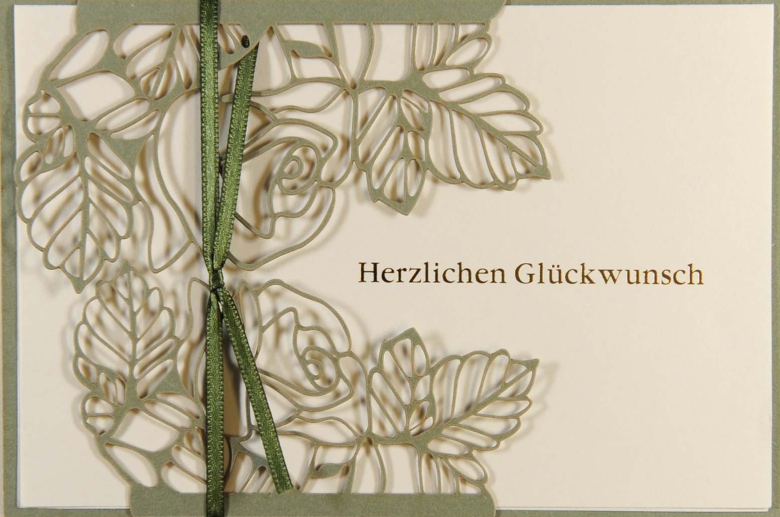 Glückwunschkarte mit Goldfolienprägung "Herzlichen Glückwunsch", filigranem, floralem Laserschnitt und grünem Satinband.