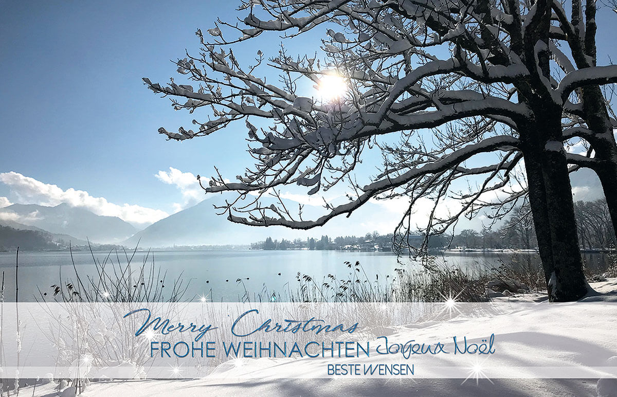 Internationale Weihnachtskarte mit verschneiter Seenlandschaft bei blauem Himmel 