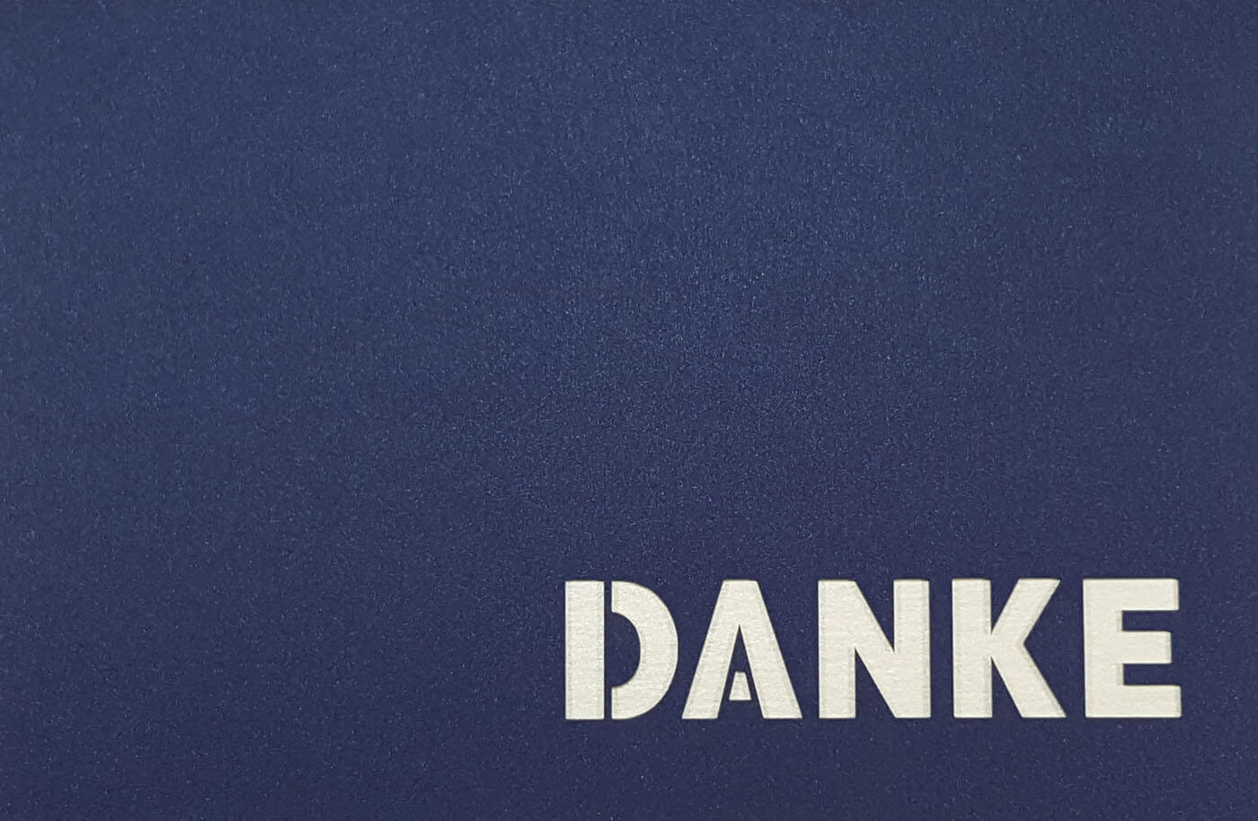 Dunkelblaue Danksagungskarte mit ausgestanztem Schriftzug "DANKE" und weißem Einlegeblatt