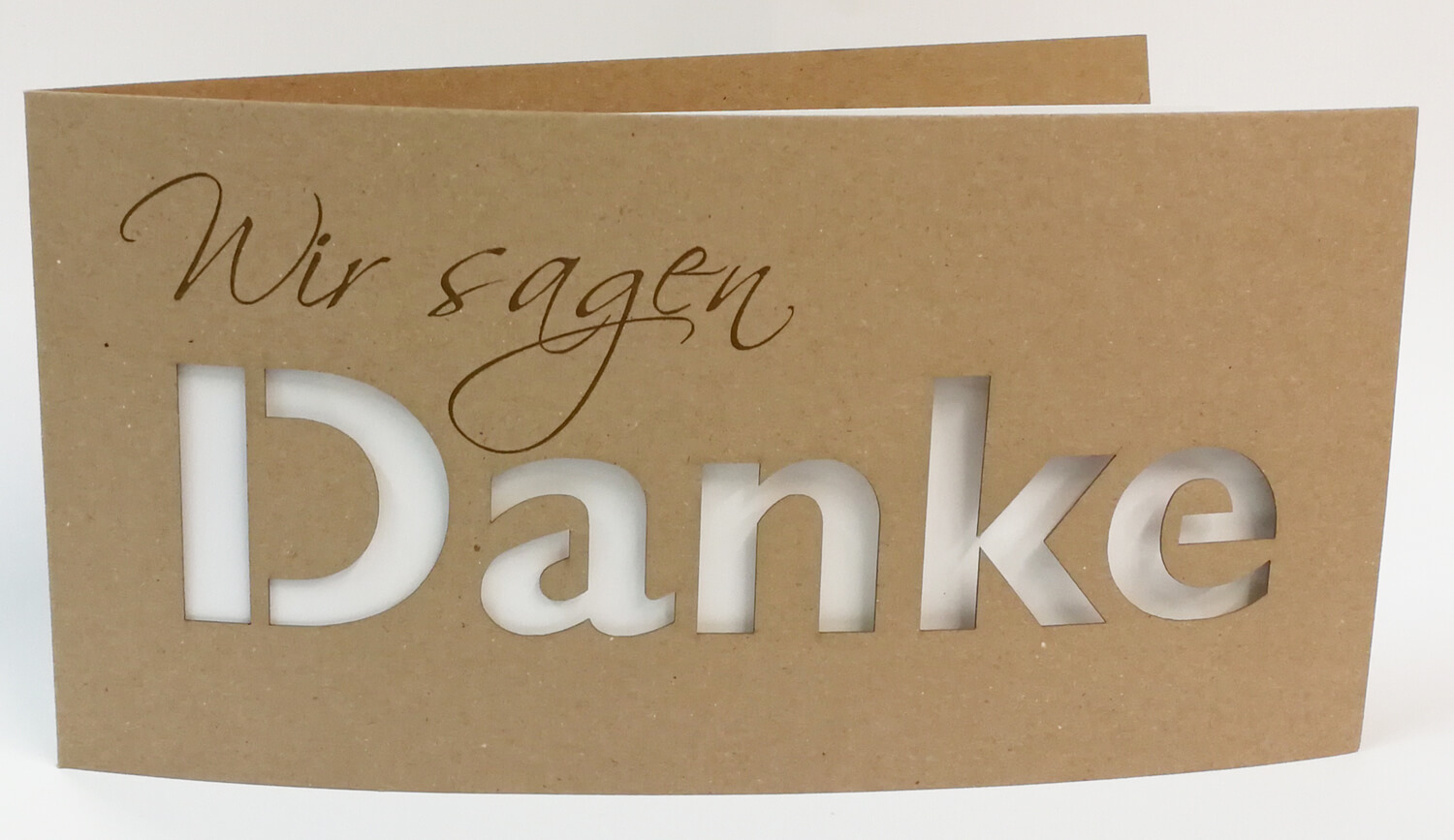 Braune Dankkarte DIN lang mit gedrucktem "Wir sagen", ausgestanztem Schriftzug "DANKE" und cremefarbenem Einlegeblatt