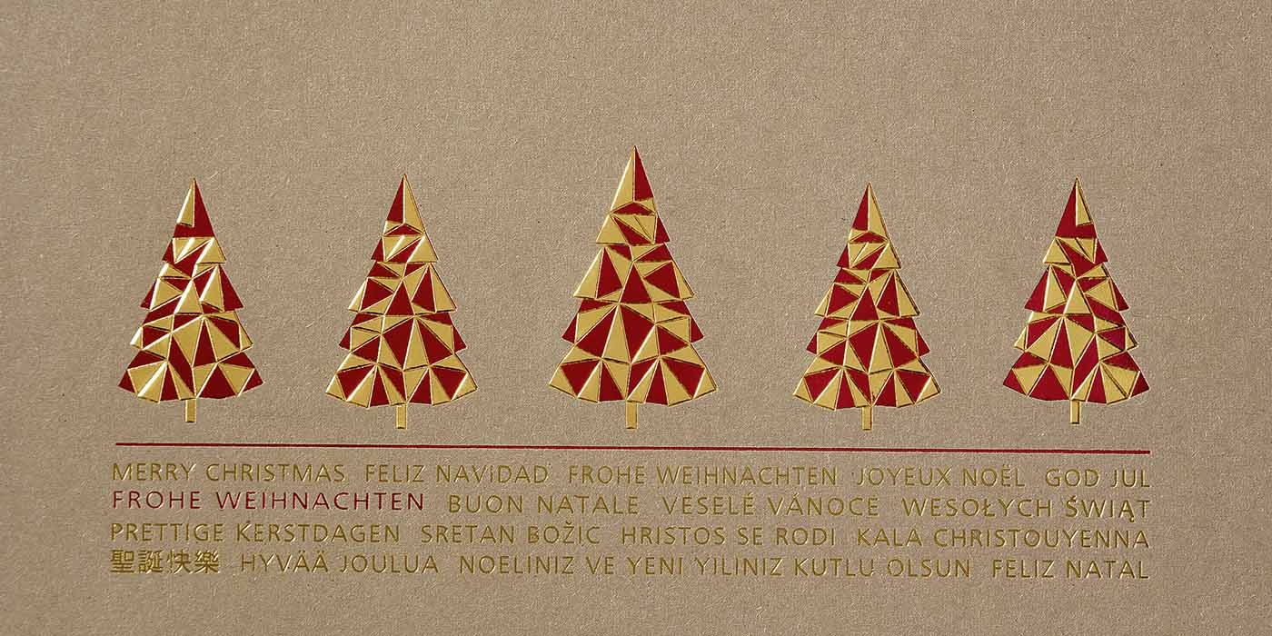 Weihnachskarte aus braunem Kraftkarton mit rot-goldener Folienprägung und internationalen Grüßen