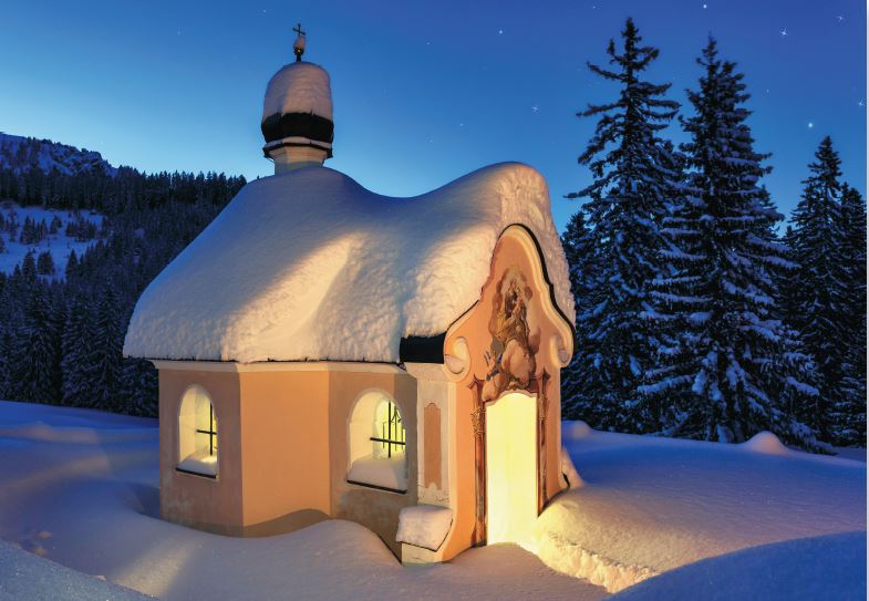 Winterliche Grußkarte mit verschneiter Bergkapelle bei sternenklarer Nacht in den Bergen