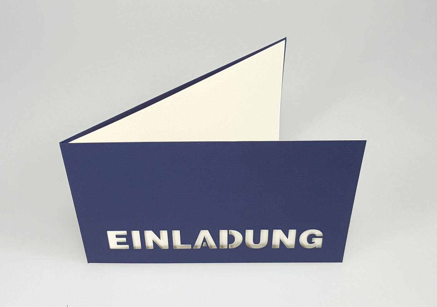 Dunkelblaue Einladungskarte mit ausgestanztem Schriftzug "EINLADUNG" und weißem Einlegeblatt - Aufgestellte Ansicht